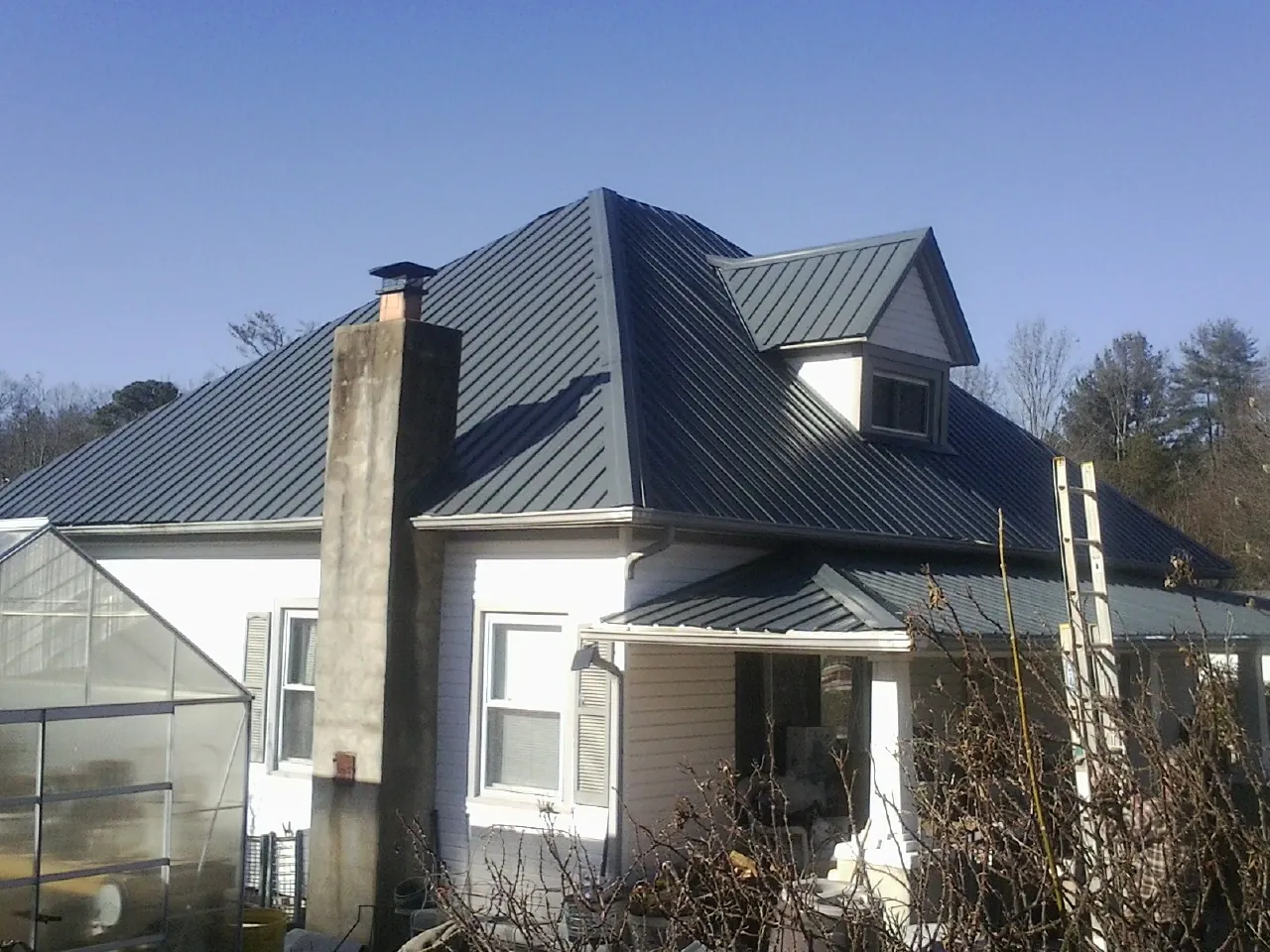 Dark blue standing seam metal roof on a white farmhouse with dormer — Slate & Tile Roof Repair by Roofing Brothers in Chemung