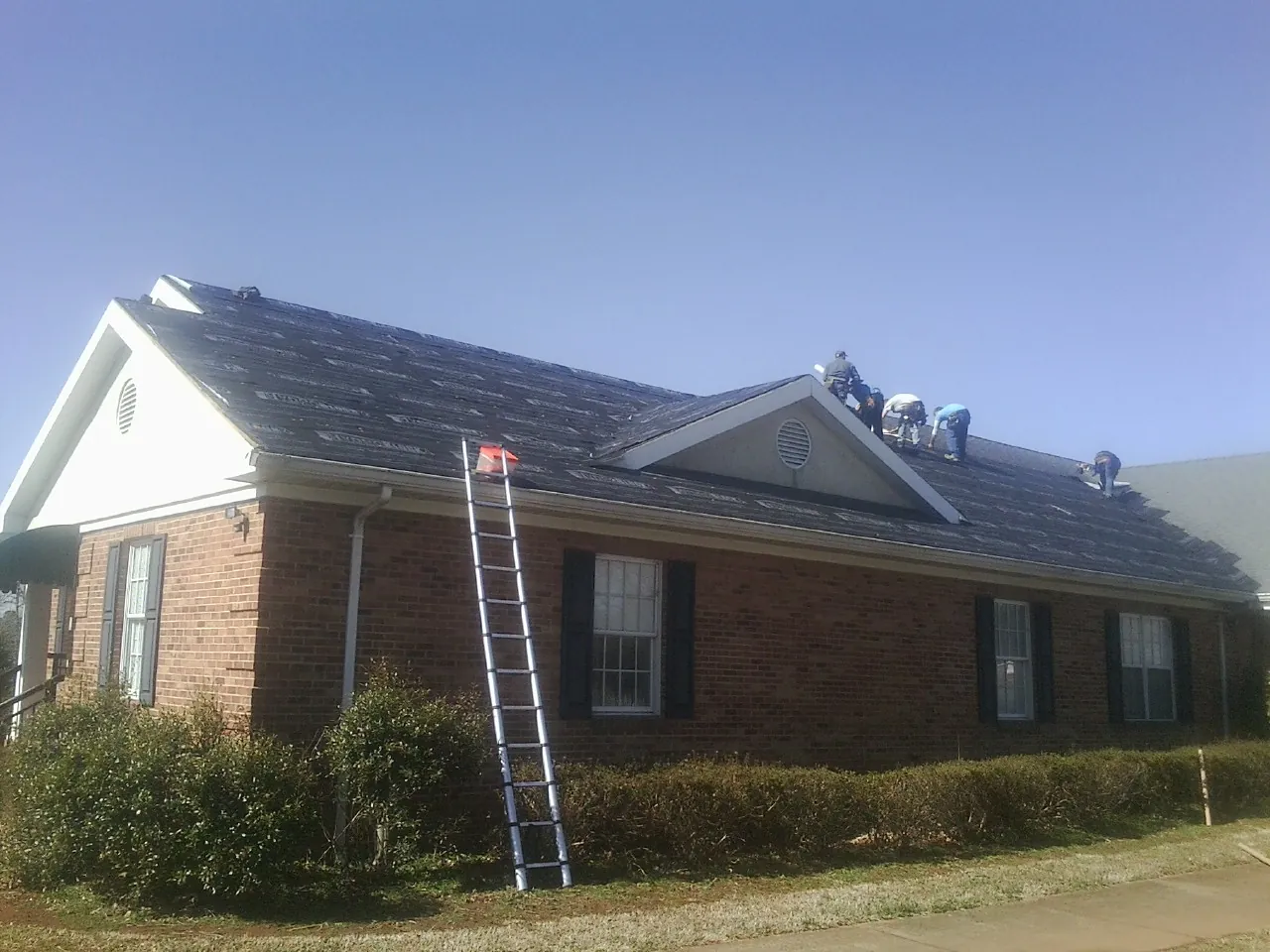 Crew tearing shingles off a brick ranch roof with a ladder set — Metal Roof Repair work by our crew in Chemung