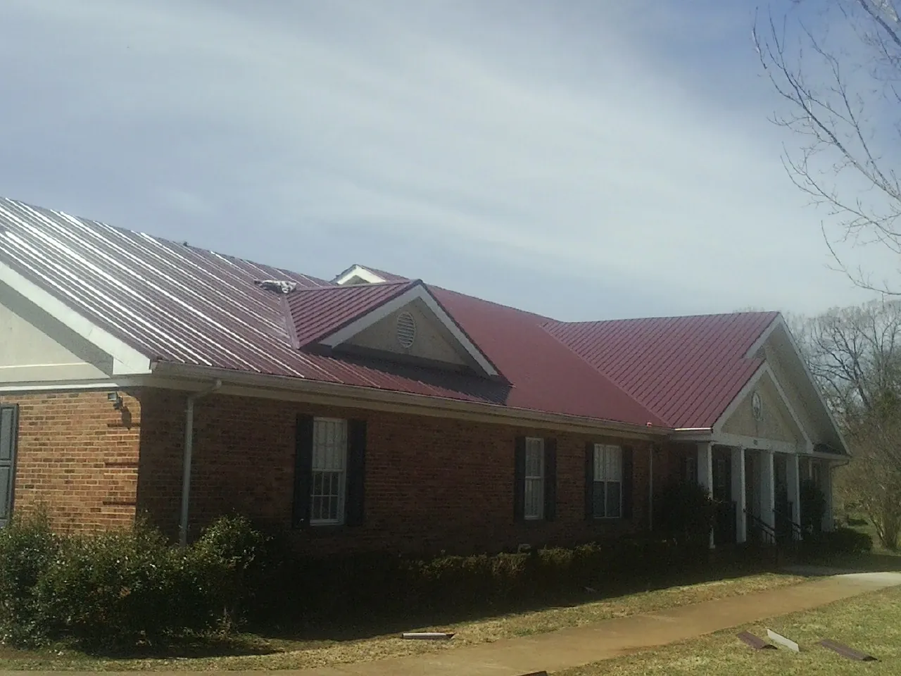 Red metal roof with gabled entries on a long brick building, from a Hail Damage Roof Repair job in Chemung