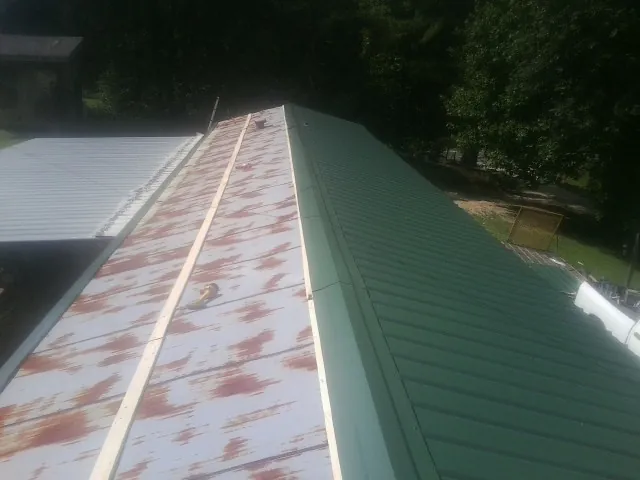 Old rusted panels beside newly installed green metal roofing — Wind Damage Roof Repair by Roofing Brothers in Chemung