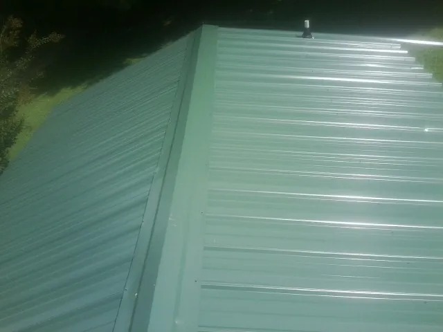New green metal panels meeting at the ridge of a roof — Flat Roof Repair work by our crew in Chemung