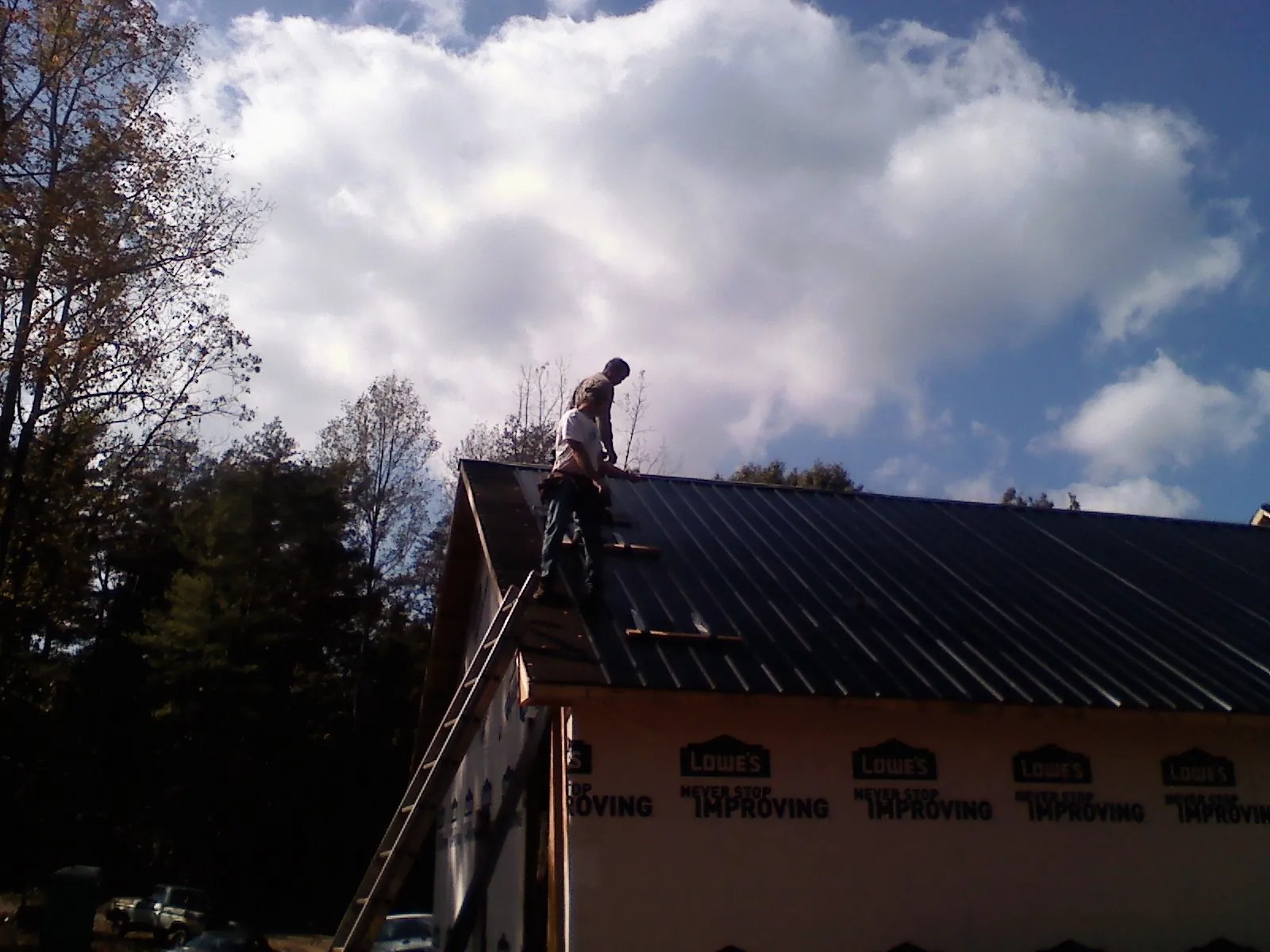 Roofer fastening dark metal panels high against a cloudy sky, from a Roof Inspection job in Chemung