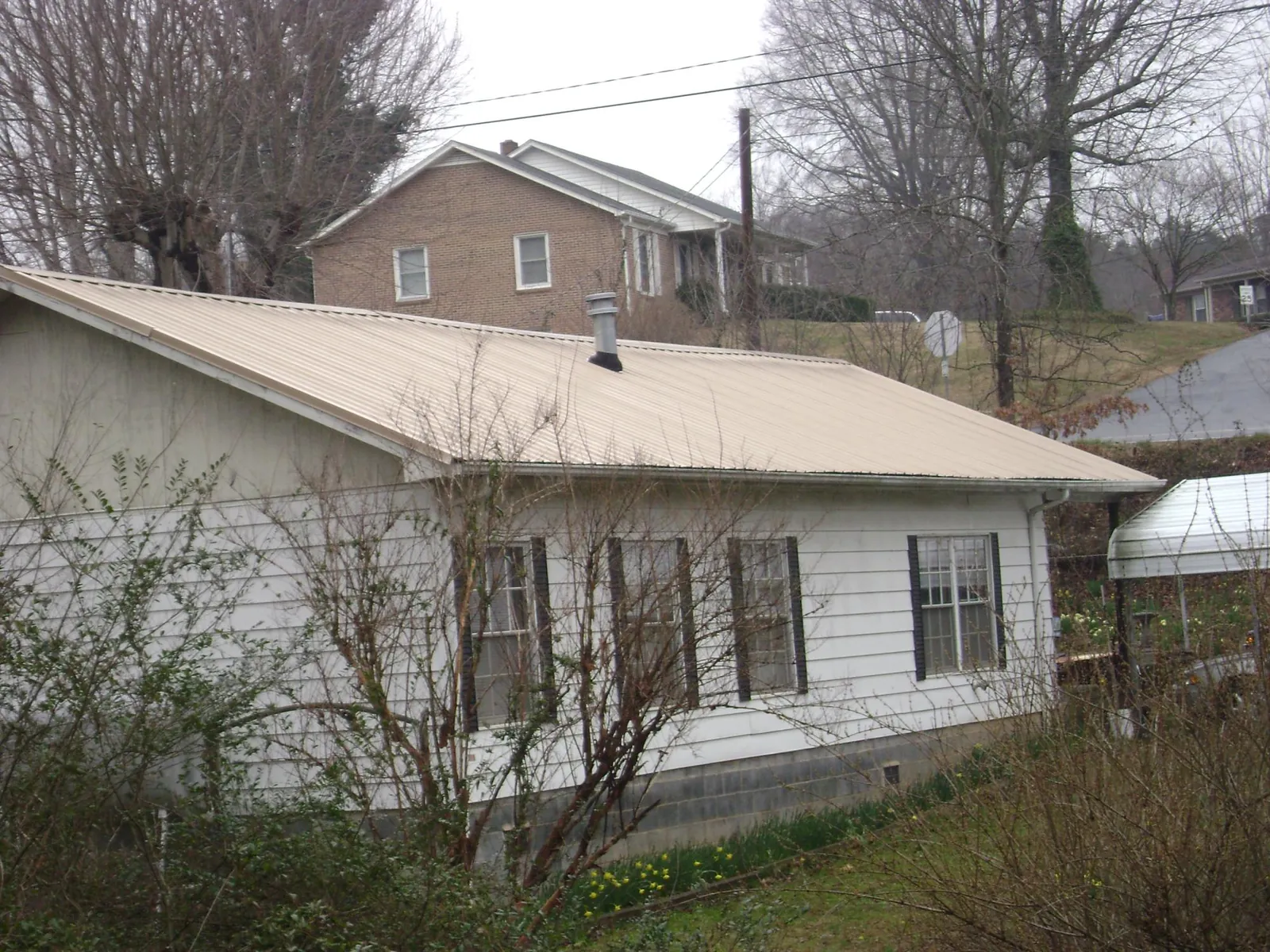 Tan metal roof on a white sided house set into a hillside — Commercial Roofing by Roofing Brothers in Chemung