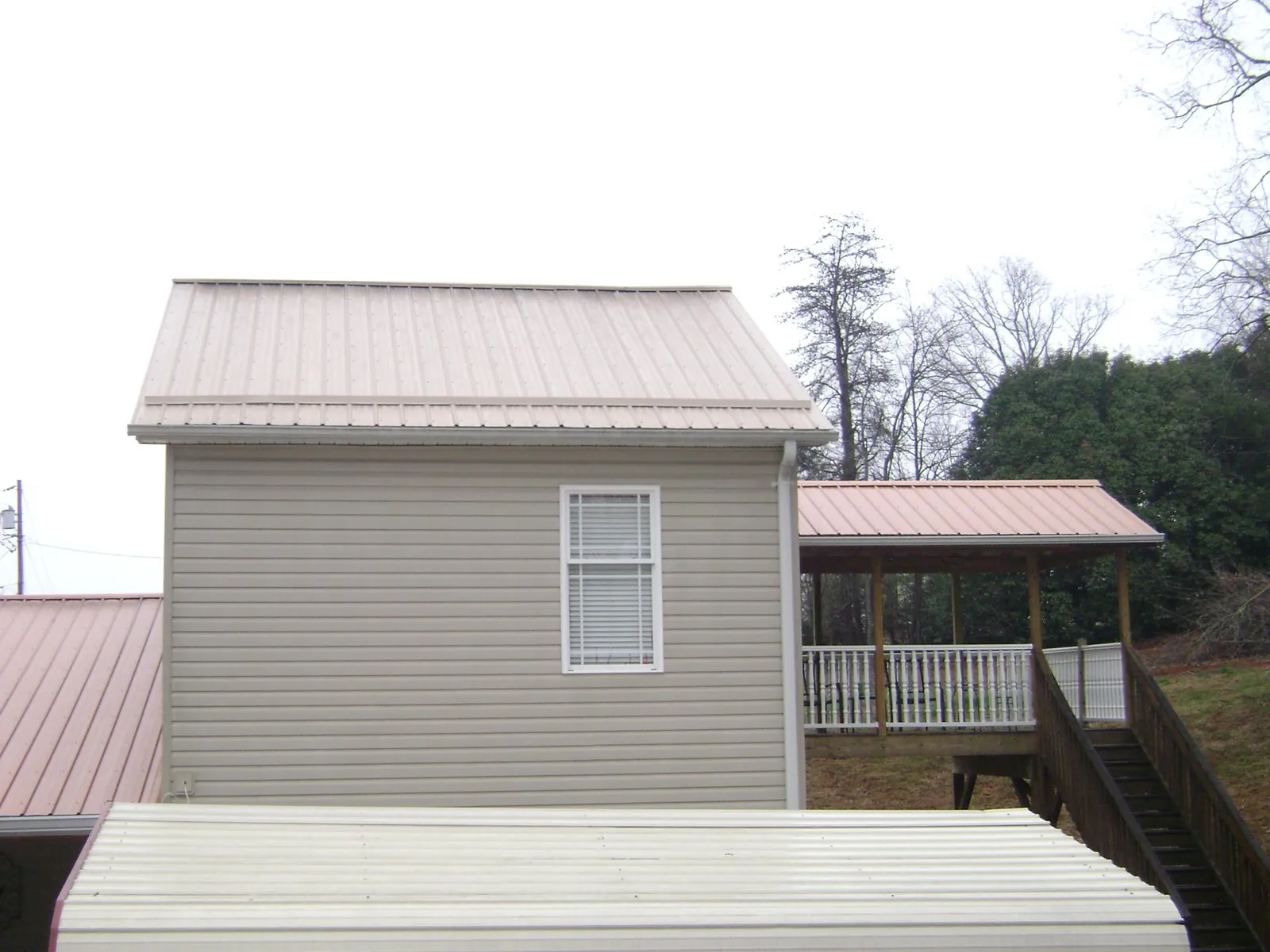 Tan metal roofs on a two story addition and attached porch, from a Roof Replacement job in Chemung